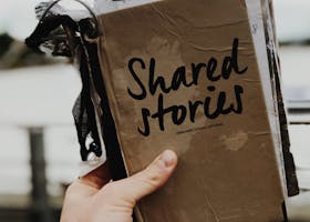 pexels-photo-2954199-2954199 Hand holds a "Shared Stories" journal against a blurred outdoor backdrop, emphasizing creativity and personal storytelling.